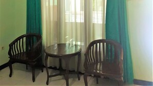 A room with two wooden chairs and a small round table, a window with curtains, and a tiled floor. - Hotel Mulia (Baki)