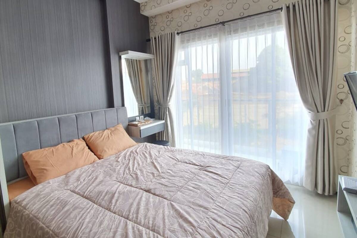 A modern bedroom with a large bed, a nightstand, a mirror, and a window with curtains.