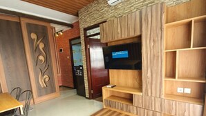 Een moderne woonkamer met een houten vloer, een grijze bank, een aan een houten muur bevestigde televisie en een bakstenen muur.