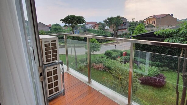 Een balkon met uitzicht op een woonwijk, een metalen hekwerk en een airconditioning.