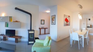A modern living room with a TV, a fireplace, a dining area with a table and chairs, and a kitchen with cabinets and a window. - Villetta sogno sul lago (Tremosine)
