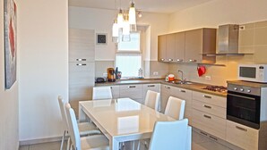 A modern kitchen with white cabinetry, a dining table with chairs, and a built-in oven. - Villetta sogno sul lago (Tremosine)