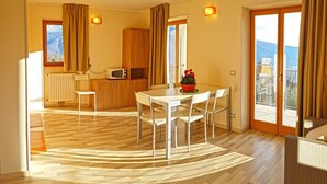 A modern kitchen with a microwave, wooden cabinets, and a dining area with a table and chairs. - Teresa Appartamento Vista (Tremosine)