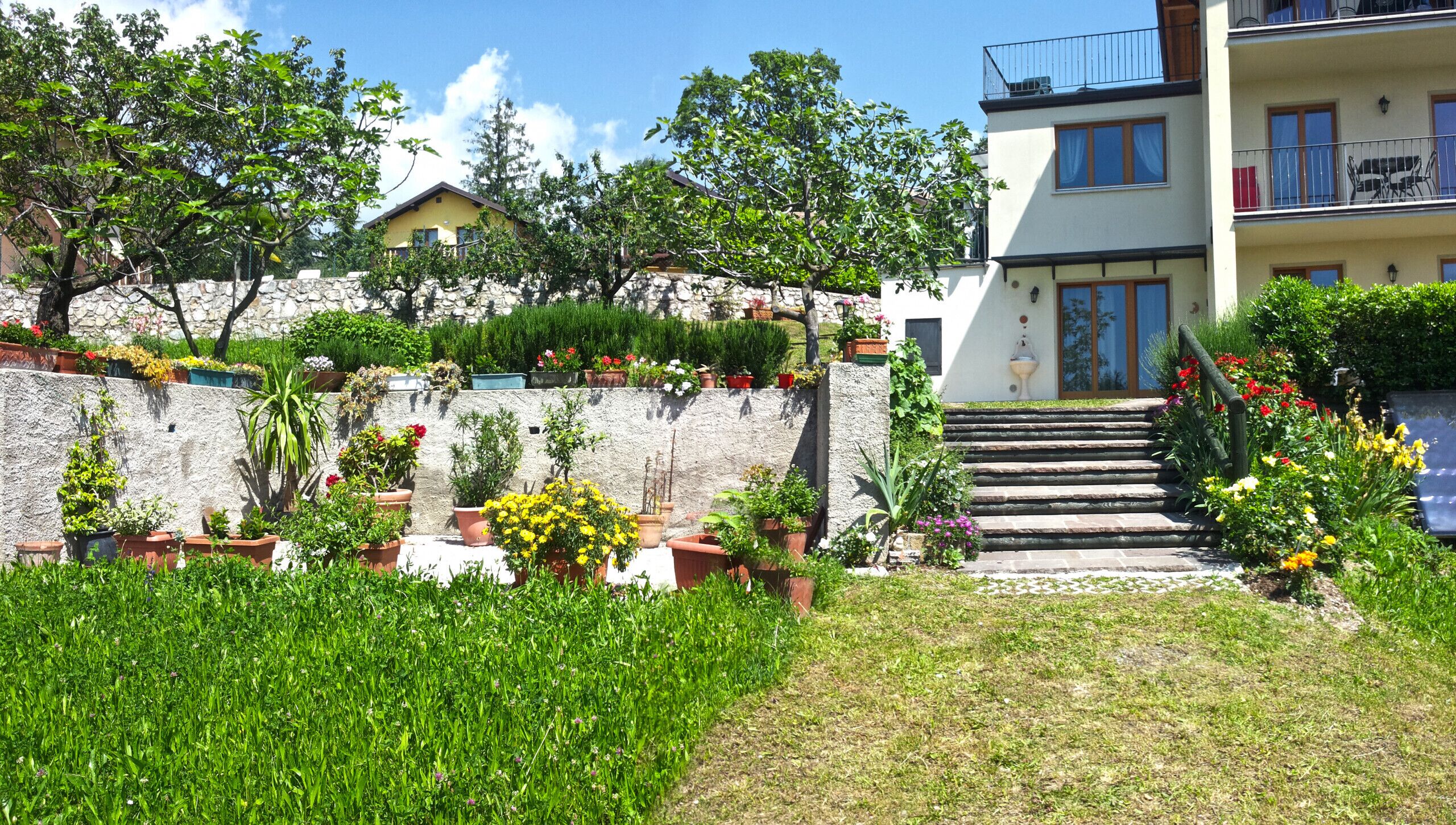 Un immeuble à plusieurs étages doté d’un mur en pierre et d’un espace jardin agrémenté de plantes et de fleurs en pot.