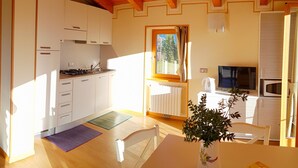 A compact kitchen with white cabinets, a stove, and a microwave. There's a dining area with a table and chairs, and a potted plant on the table. - Teresa Attico Vista (Tremosine)