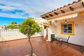 A covered patio with a tiled floor, a small tree, and a table with chairs. - CH Estaca Playa Flamenca (Orihuela Costa) (Orihuela Costa)