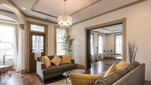 A spacious living room with a dark brown sofa, a round coffee table, and a chandelier. There is a large window providing natural light and a view of the outside. - Elegant, King Bed, Privacy,  Free Parking (Washington)