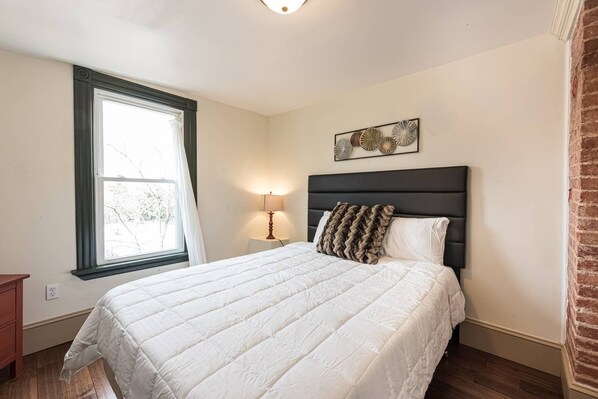 A bedroom with a bed, a nightstand, a lamp, a window, and a wall art piece. - Elegant, King Bed, Privacy, Free Parking (Washington)