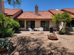 A building with a red-tiled roof, a patio with a table and chairs, and a cactus plant. - Pet Friendly Omni Golf Course Views from Open floor plan with yard-garage (Tucson)