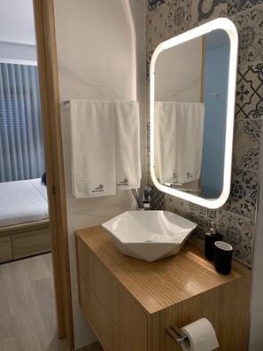 A modern bathroom with a white sink, a mirror with a light, and patterned tiles. - Casa do Recife: Apartment (Viana do Castelo)