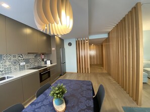 A modern kitchen with a patterned backsplash, a built-in oven, and a refrigerator. There is a dining area with a table and chairs, and a potted plant on the table. - Casa do Recife: Apartment (Viana do Castelo)