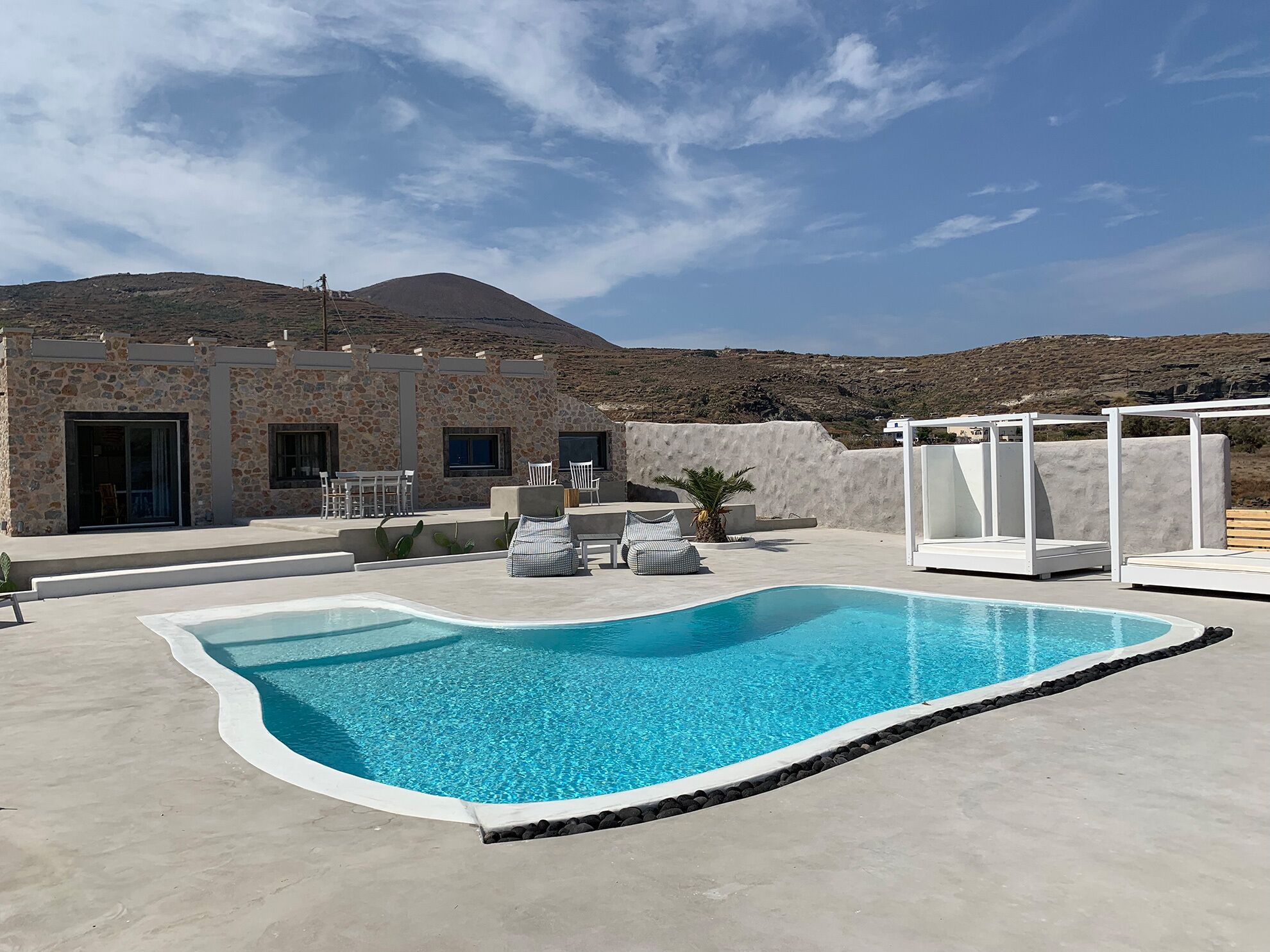 A pool area with a stone building, outdoor seating, and a view of a mountain.