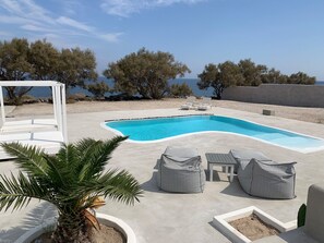 A swimming pool with lounge chairs and a palm tree. - Villa Beltramo (Santorini)