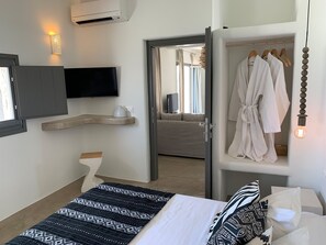 A hotel room with a bed, a TV, a robe rack, and a mirror. - Villa Beltramo (Santorini)