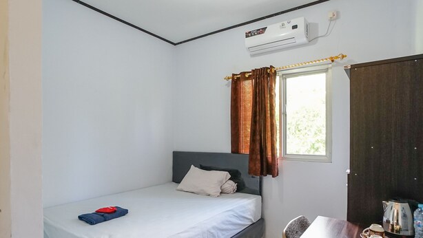 A small, clean room with a single bed, a table with a kettle and cups, and a window with curtains.