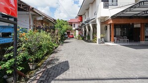 A paved street with buildings on either side, a red car in the distance, and a red sign with white text. - PAS Residence (Manado)