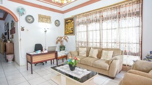 A living room with a sofa, coffee table, and a desk with a computer. There is a window with curtains and a chandelier. - PAS Residence (Manado)