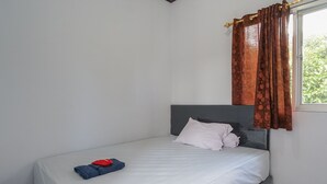 A single bed with a grey headboard, white bedding, and a window with brown curtains.