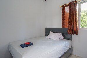 A single bed with a grey headboard, white bedding, and a window with brown curtains.