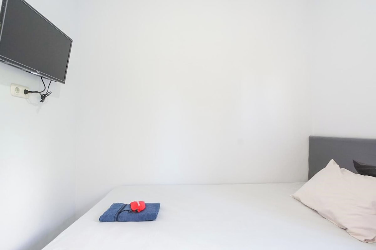 A single bed with a grey headboard, a white wall, and a mounted television.