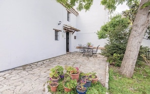 A white building with a stone-paved courtyard, a table with chairs, and potted plants.