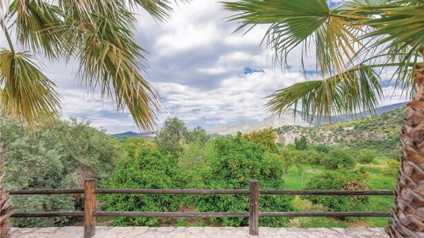 Un muro de piedra con valla de madera, con vistas a un paisaje verde y exuberante, con árboles y una cadena montañosa distante.