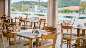 A restaurant with wooden tables and chairs, large windows with a view of a hilly landscape. - Tri Hotel São João Batista (Sao Joao Batista)