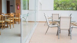 A modern indoor dining area with wooden chairs and tables, a glass partition, and a view of trees outside. - Tri Hotel São João Batista (Sao Joao Batista)