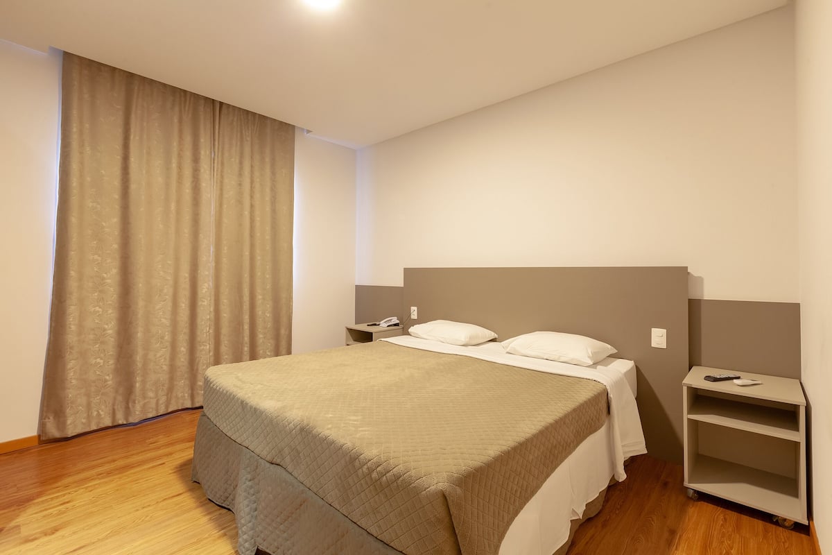 A hotel room with a large bed, a nightstand, a desk, and a wardrobe.