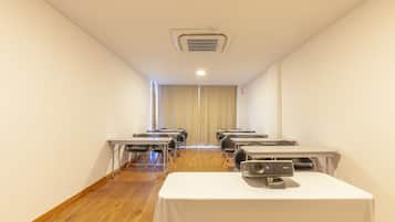Un salón de conferencias con filas de mesas, un proyector y una rejilla en el techo.