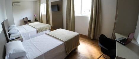 Habitación de hotel con dos camas, un escritorio con una computadora portátil, una silla y un televisor en la pared.