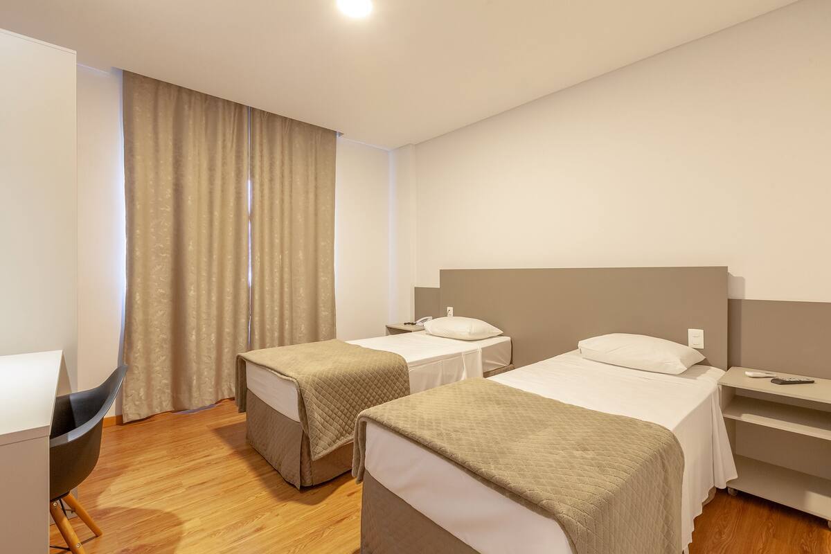 A hotel room with two beds, a desk, a chair, and a window with curtains.