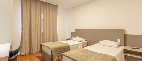 A hotel room with two beds, a desk, a chair, and a window with curtains.