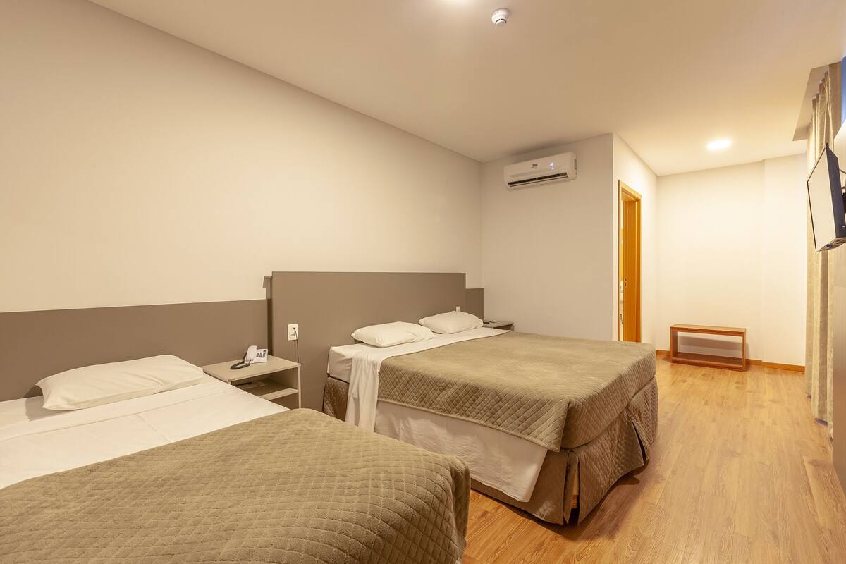 A hotel room with two beds, a bedside table with a phone, an air conditioning unit on the wall, and a wooden floor.