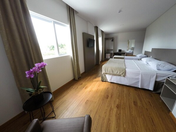 Habitación de hotel con dos camas, un escritorio, una silla, televisión y ventana con cortinas.