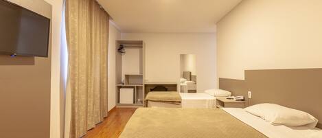 A hotel room with a bed, a desk, a chair, a television, and a wardrobe.