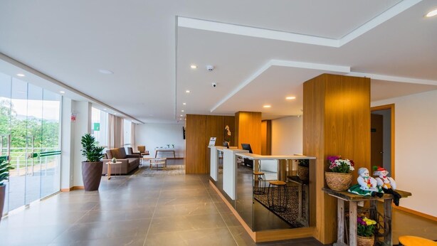 A modern hotel lobby with a reception desk, seating area, and large windows offering a view of the outdoors. - Tri Hotel São João Batista (Sao Joao Batista)