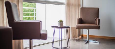 Una habitación moderna con dos sillones de cuero marrón, una mesita redonda con una planta en maceta y amplias ventanas con cortinas.