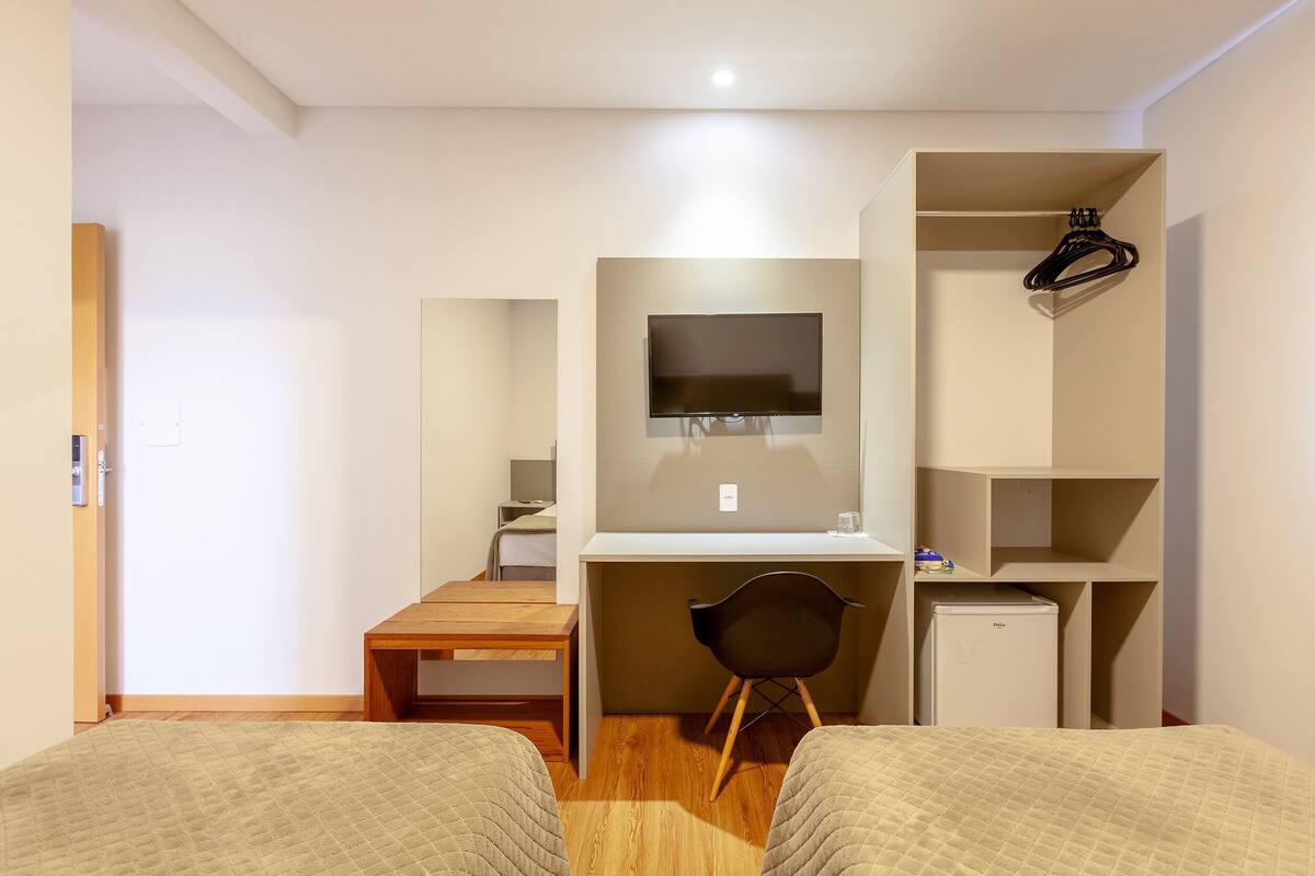 A bedroom with two beds, a desk, a chair, a TV, a wardrobe, and a small refrigerator.