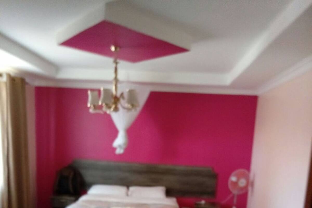 A bedroom with a bed, bedside table, chair, and a standing fan.