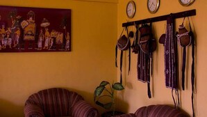 Una habitación con pared amarilla, un cuadro de figuras tradicionales, un reloj y un perchero de pared con bolsos y accesorios.