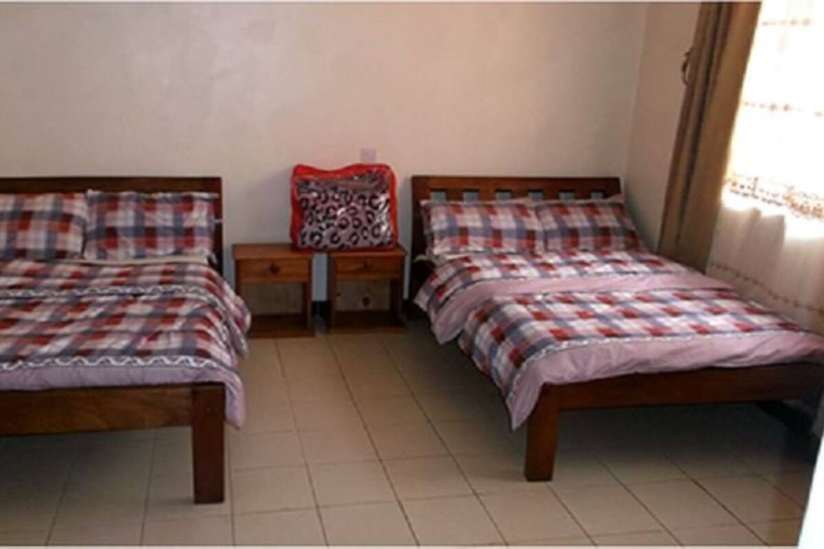 A room with two beds, each with a plaid bedspread, a nightstand with a lamp, and a red pillow.