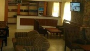 Un amplio salón con diversas opciones de asientos, incluyendo sofás y sillones, dispuestos alrededor de una mesa de centro. Hay un televisor montado en la pared, y la habitación tiene un ambiente cálido y acogedor, con luz natural entrando por las ventanas.