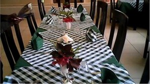 Una mesa de comedor con mantel a cuadros, servilletas verdes y un florero con flores.