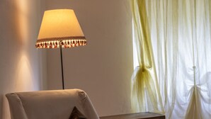 A room with a chair, a lamp, a wooden nightstand, and sheer curtains. - Agritourism San Carlo - apartment Trilo1 (Pomarance)