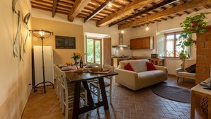 A spacious living area with a wooden ceiling, a dining table with chairs, a white sofa, and a kitchen in the background. - Agritourism San Carlo - apartment Trilo1 (Pomarance)