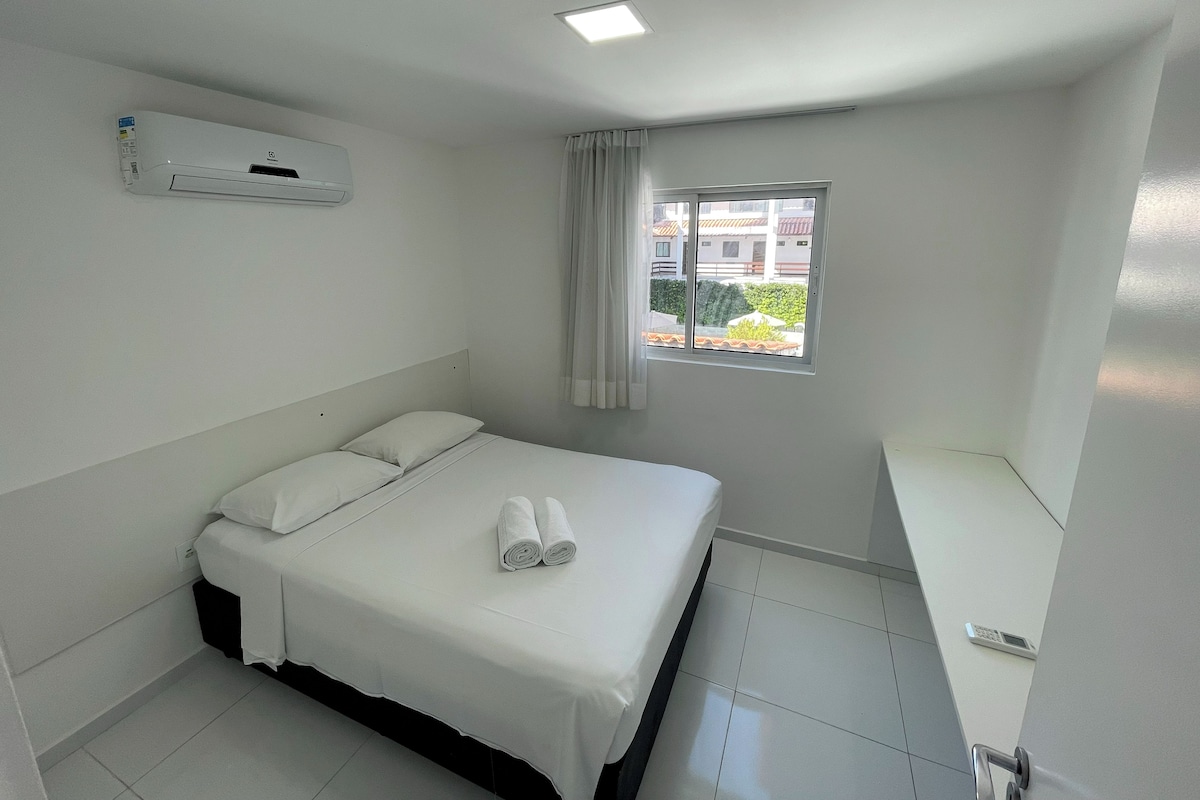 Habitación de hotel con cama, ventana con cortinas, luz de techo y aire acondicionado instalado en la pared.