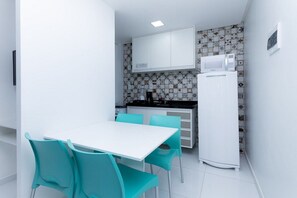 A compact kitchen with white cabinets, a microwave, and a refrigerator. There is a white table with turquoise chairs. - Porto Sol Flats by AFT (Ipojuca)