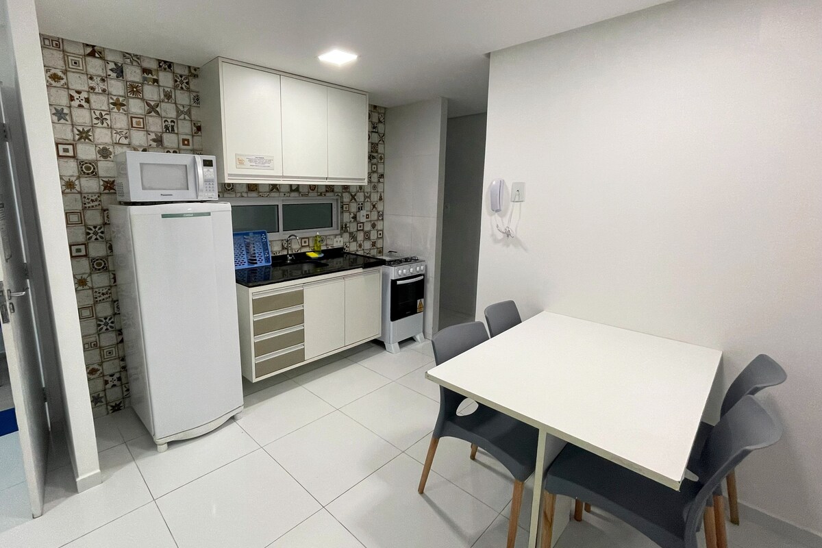 Une cuisine compacte avec des meubles blancs, un four à micro-ondes, une cuisinière et une table à manger avec des chaises.