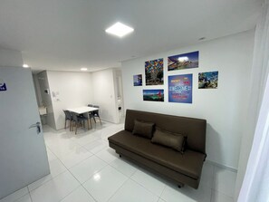 A modern living room with a brown sofa, a dining table with chairs, and a kitchen area in the background. - Porto Sol Flats by AFT (Ipojuca)